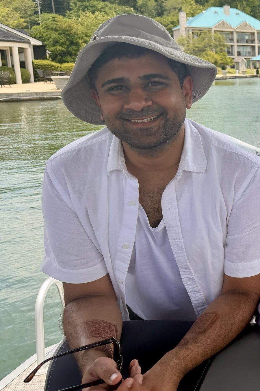 Azeem smiling on a boat, wearing a sun hat, with natural henna stains on both forearms